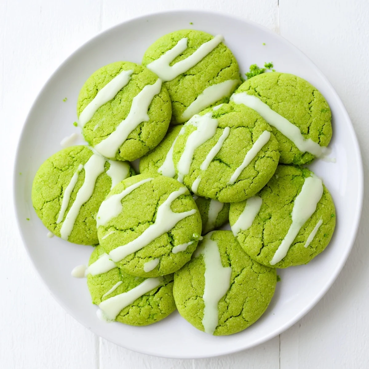 Soft green velvet cookies topped with melty white chocolate drizzle on a white plate