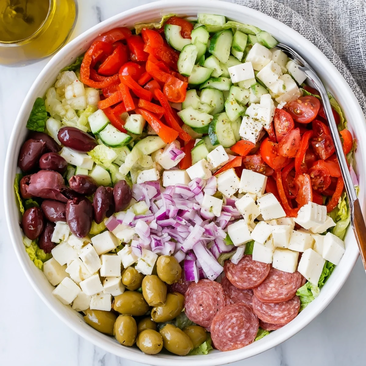 Colorful Italian chopped salad with fresh vegetables, salami, mozzarella, olives, and zesty homemade dressing in a white bowl