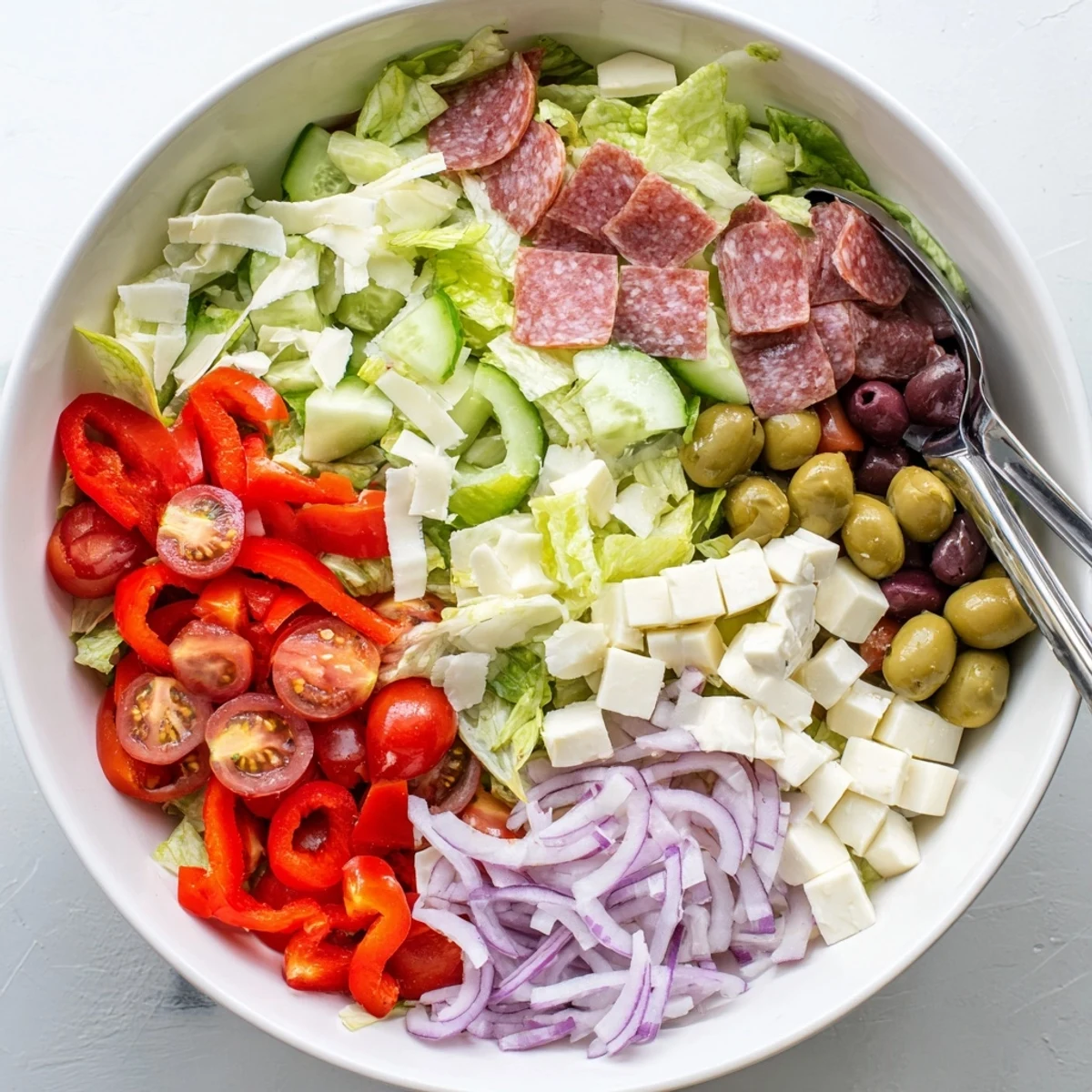 Fresh Italian chopped salad bowl loaded with crunchy vegetables, olives, Genoa salami, and cubed mozzarella in homemade dressing