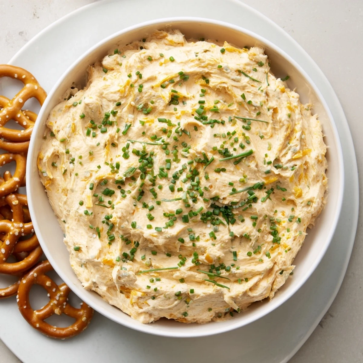Creamy savory pretzel dip topped with fresh chives, served alongside warm soft pretzels