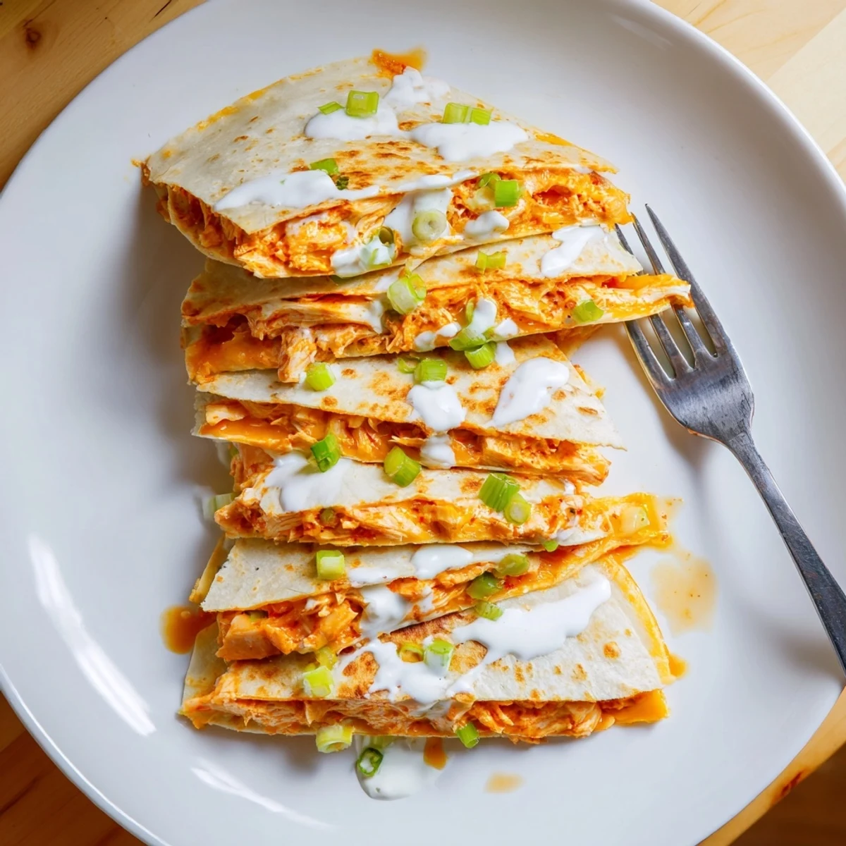Golden Buffalo chicken quesadillas sliced into wedges with creamy white ranch drizzle