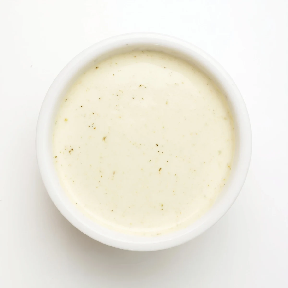 Smooth white garlic sauce bowl topped with fresh herbs beside crisp vegetable sticks for dipping