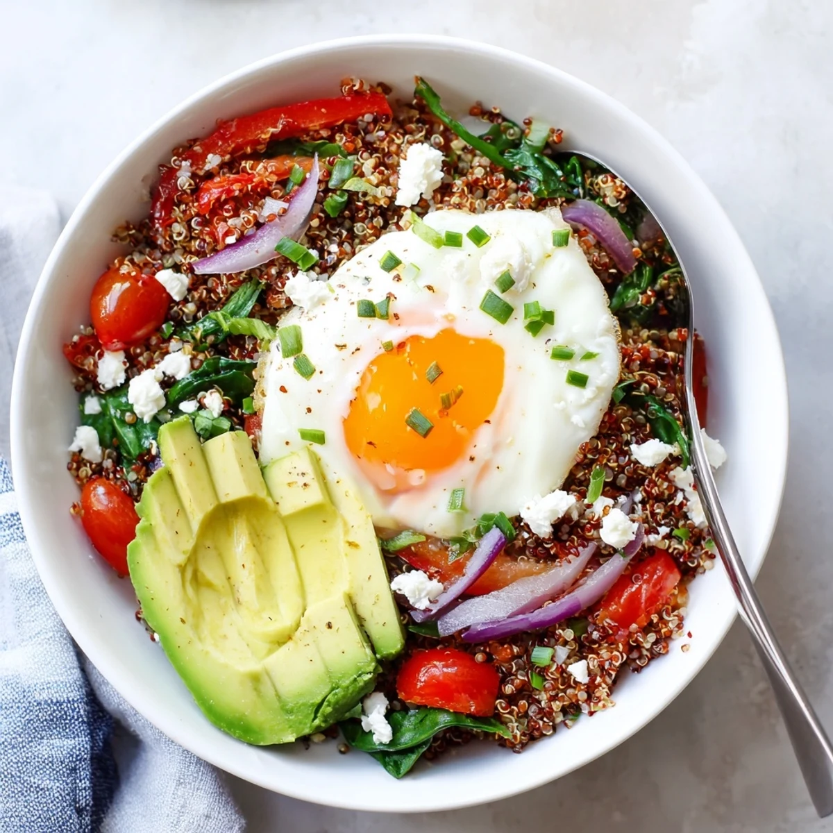 Golden fried egg resting atop fluffy savory quinoa breakfast bowl with colorful sautéed vegetables
