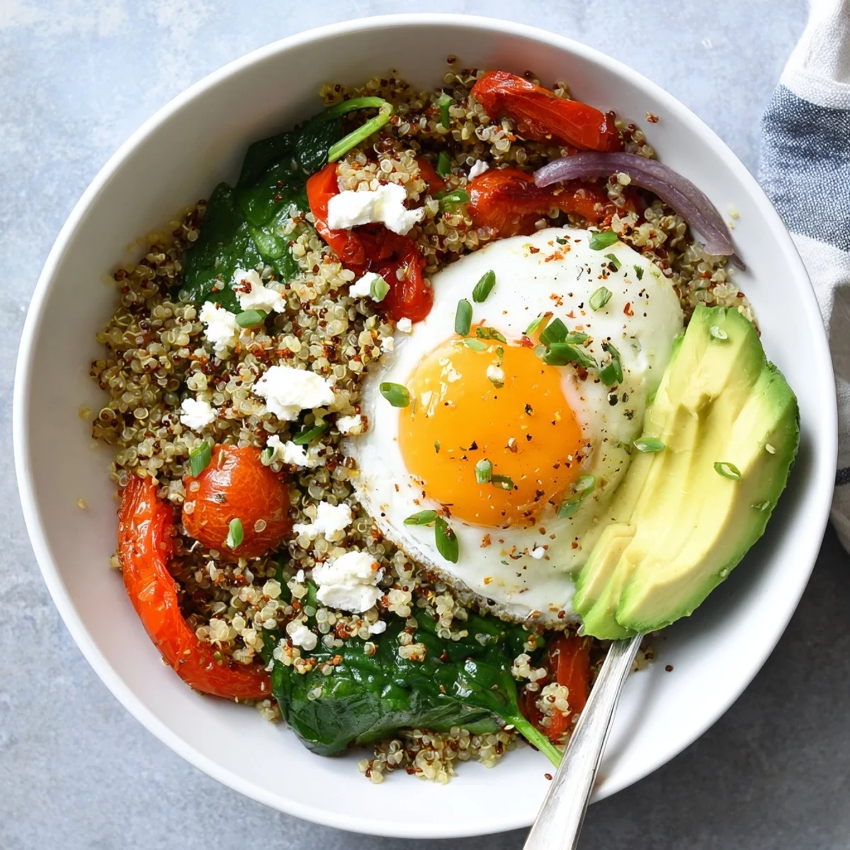 Protein-rich savory quinoa breakfast bowl topped with fried egg, fresh herbs, and avocado slices