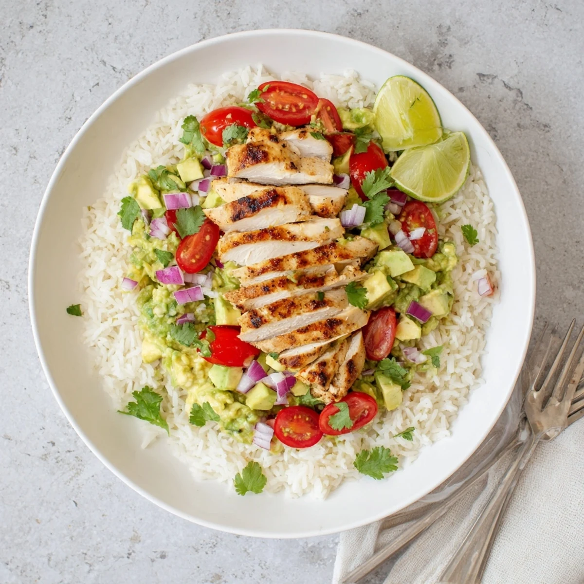Layered honey lime chicken avocado rice stack served on a white plate with red onion, cherry tomatoes, and lime wedge garnish