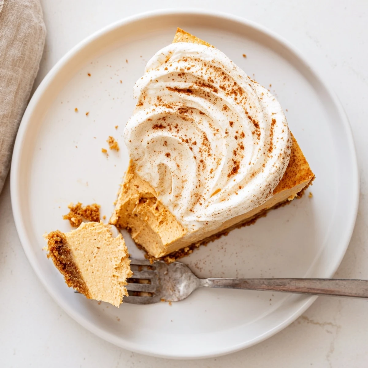 Pumpkin Spice Christmas Cheesecake slice showing creamy orange filling with cinnamon dusted whipped cream topping