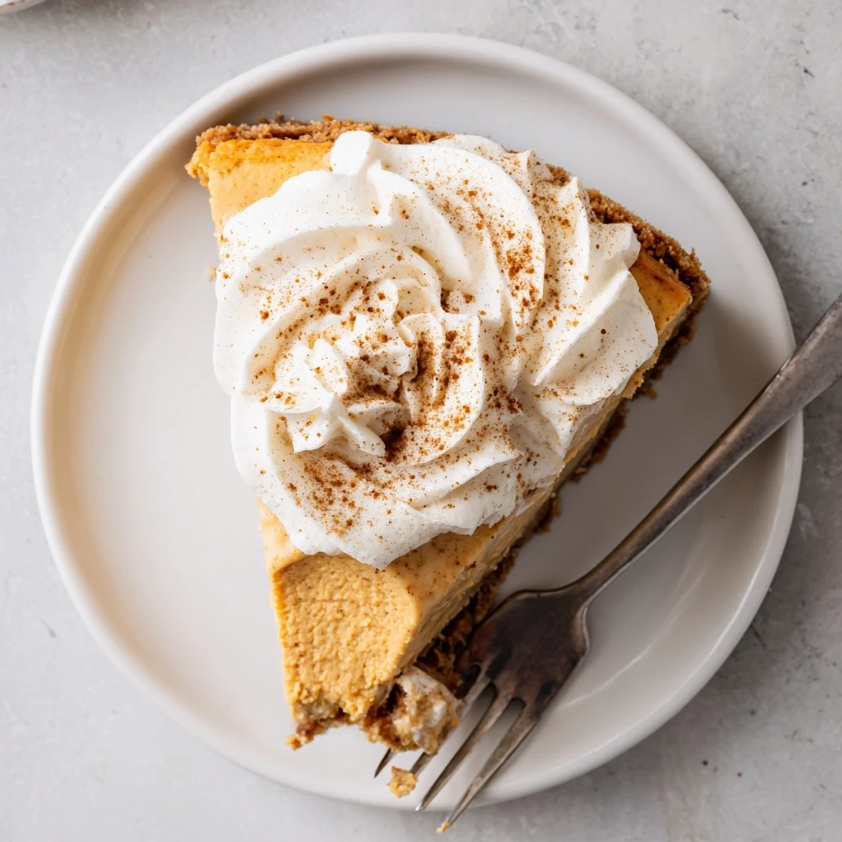 Festive Pumpkin Spice Christmas Cheesecake on a white plate garnished with ground cinnamon and holiday spirit