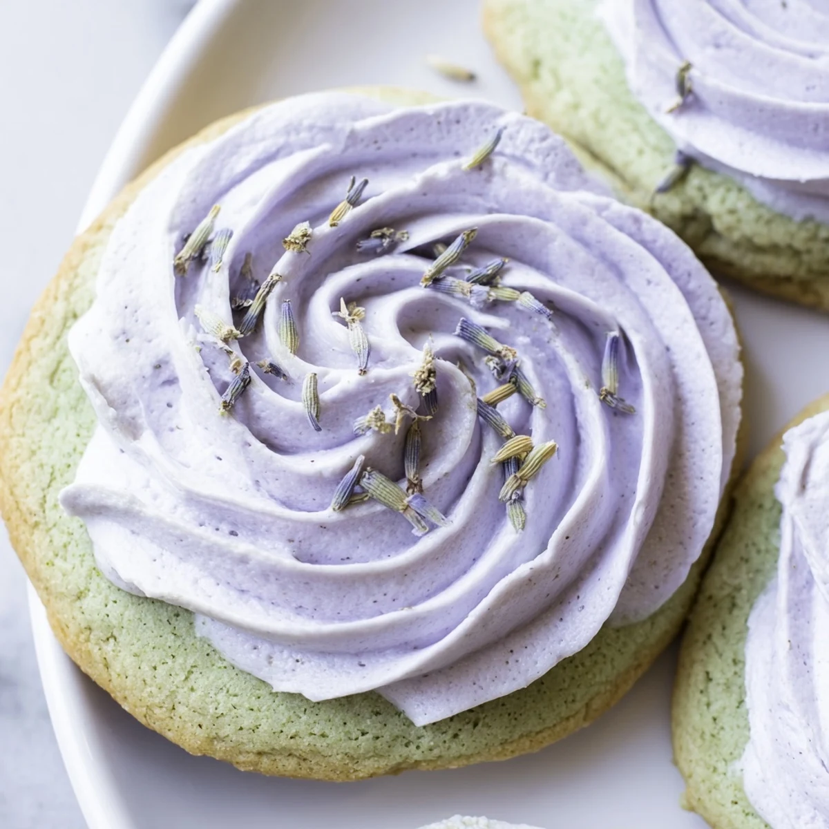 Matcha sugar cookies with lavender frosting arranged on a rustic white serving plate