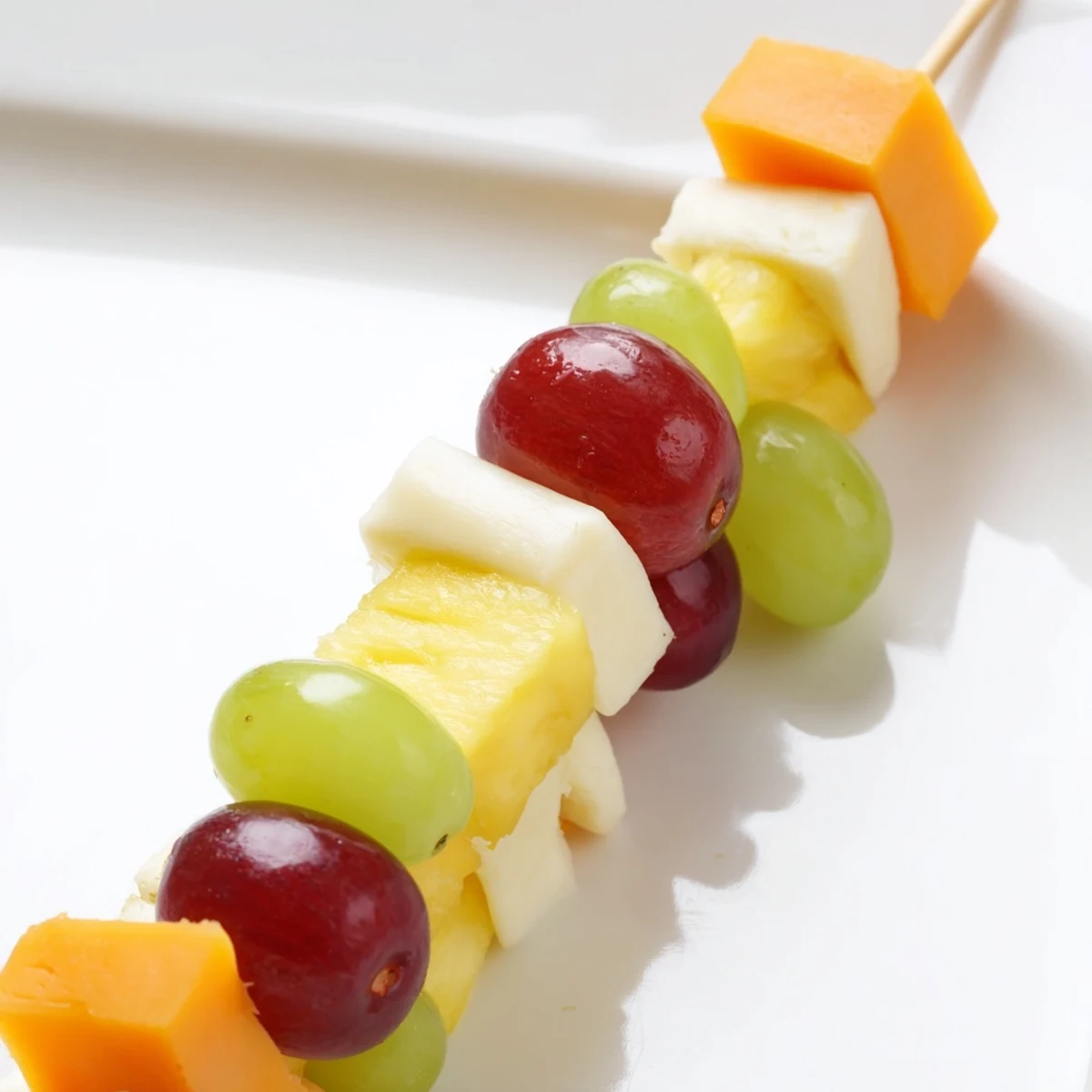 Colorful fruit and cheese kabobs arranged on platter with grapes strawberries pineapple and cheddar cubes