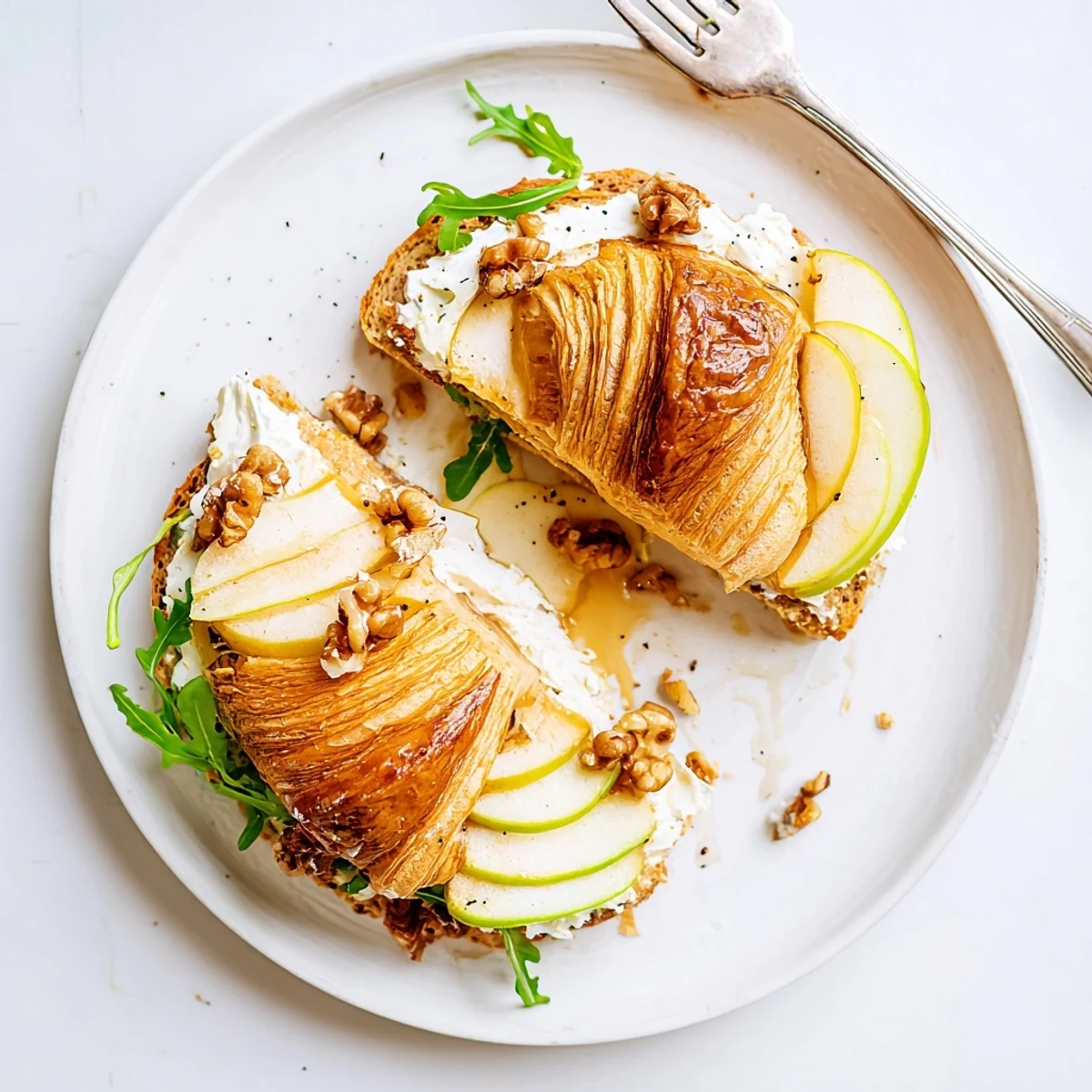 Apple Goat Cheese Croissant Sandwich on plate with arugula, drizzled honey, light brunch.
