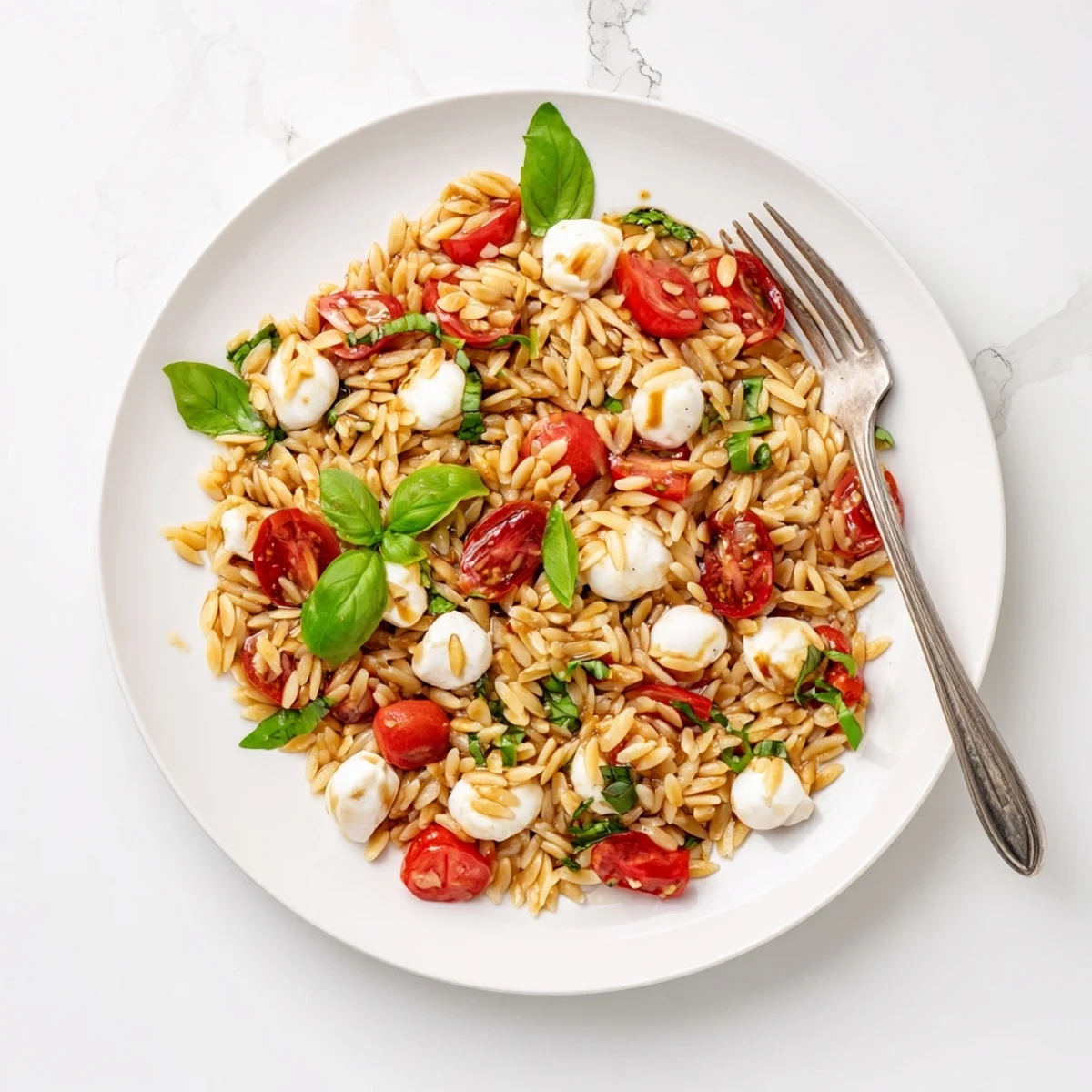 Fresh Caprese orzo pasta salad with juicy tomatoes, mozzarella pearls, and fragrant basil leaves