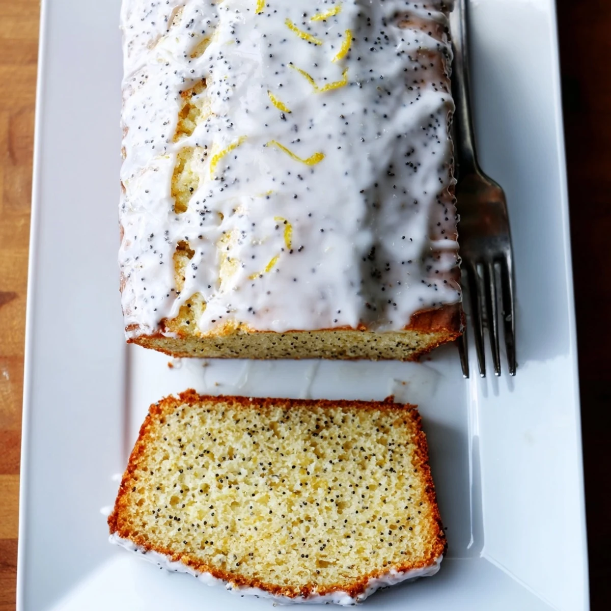 Golden lemon poppy seed loaf cake drizzled with sweet white glaze on serving plate