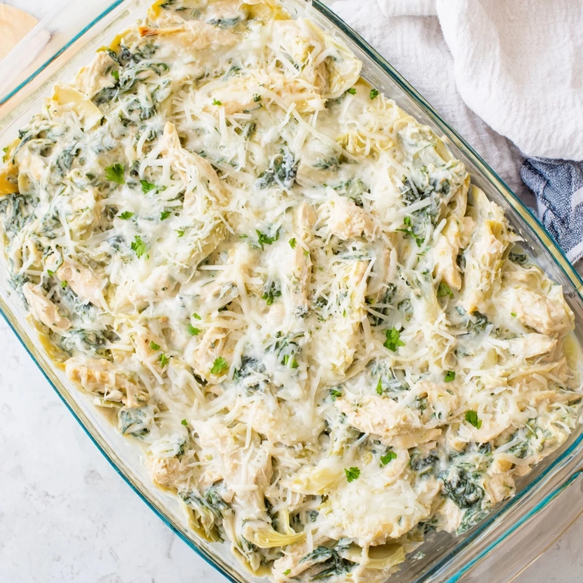 Creamy baked Spinach Artichoke Chicken Casserole served in a white ceramic dish with garnish