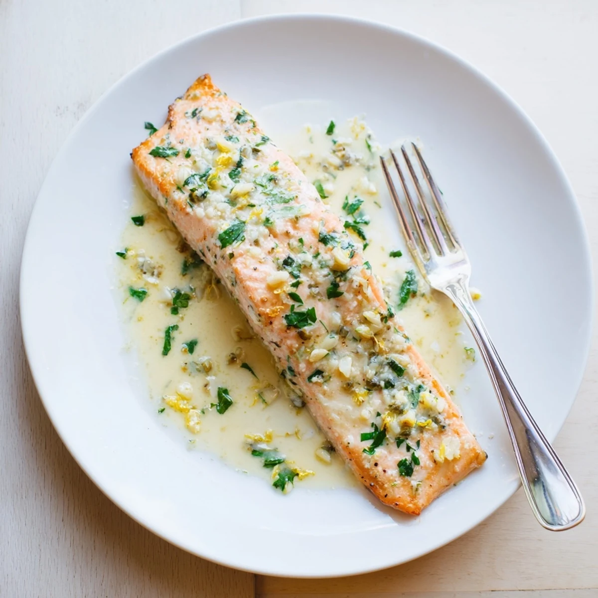Golden brown salmon topped with rich tangy lemon cream sauce served on white dinner plate
