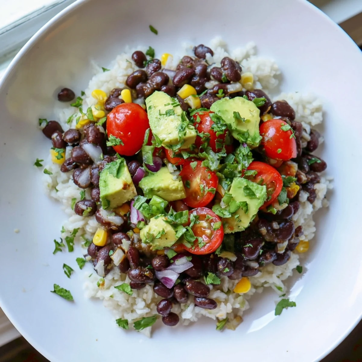Steaming black bean and rice bowl garnished with diced tomatoes and lime wedges