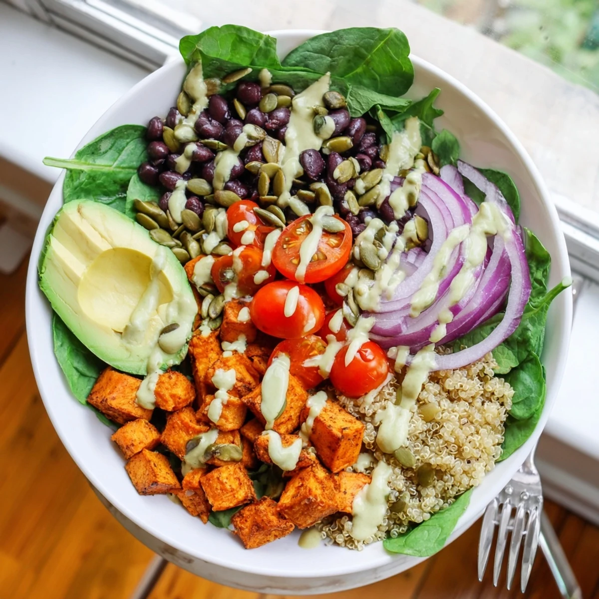 Creamy sweet potato bowl topped with avocado, black beans, and tahini dressing