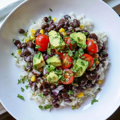 Steaming black bean and rice bowl garnished with diced tomatoes and lime wedges
