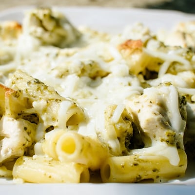 Tender chunks of chicken and penne pasta coated in creamy green pesto sauce ready for baking